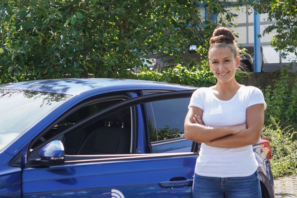 Auf dem Bild sieht man Mouna Miri neben einem Auto der Cardia Pflegeteam Flick GmbH.